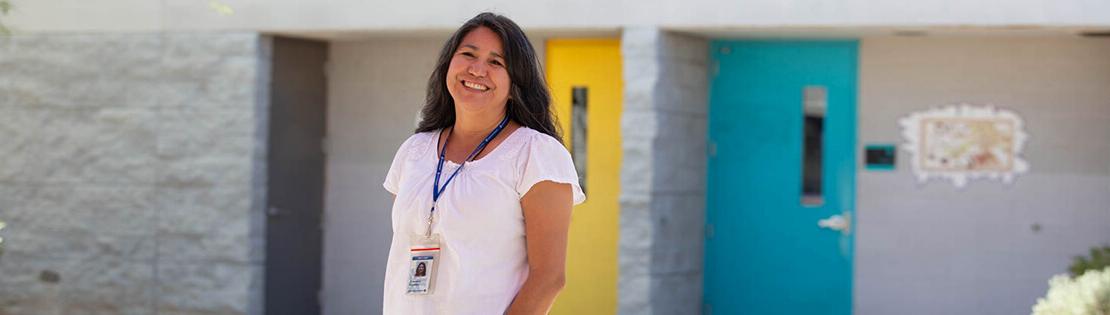 A faculty member stands smiling in front of classrooms